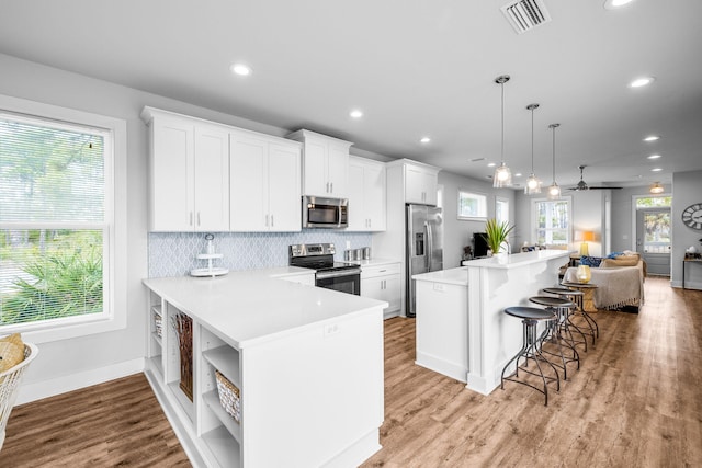 kitchen with appliances with stainless steel finishes, pendant lighting, white cabinets, and a kitchen bar