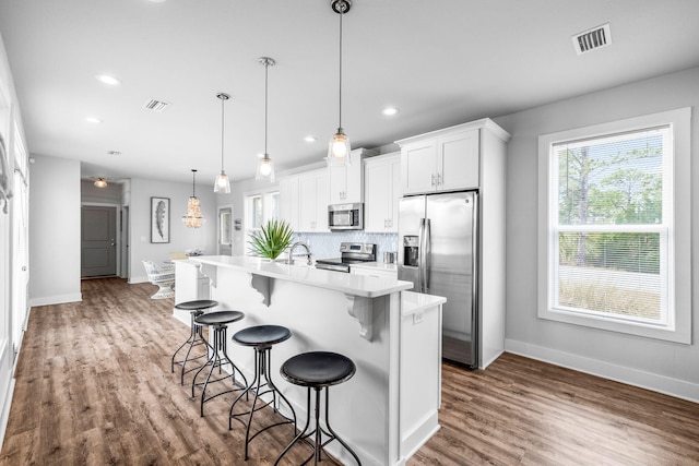 kitchen featuring pendant lighting, a kitchen breakfast bar, stainless steel appliances, an island with sink, and white cabinets