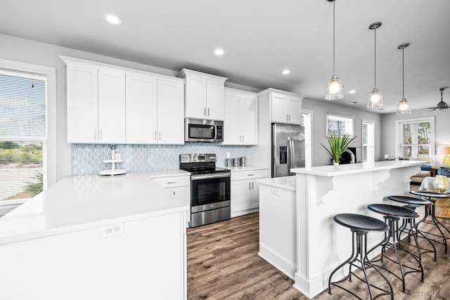 kitchen featuring white cabinets, a kitchen bar, hanging light fixtures, a center island, and stainless steel appliances