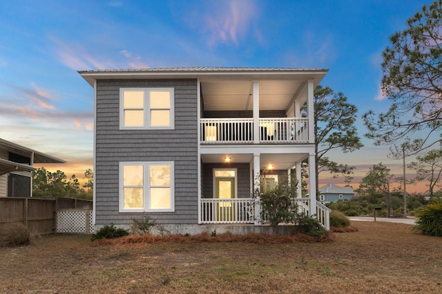 back house at dusk with a porch, a balcony, and a yard