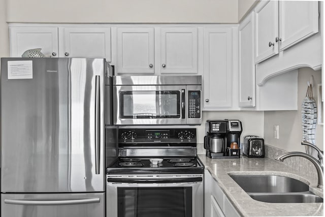 kitchen featuring stainless steel appliances, white cabinetry, sink, and light stone counters