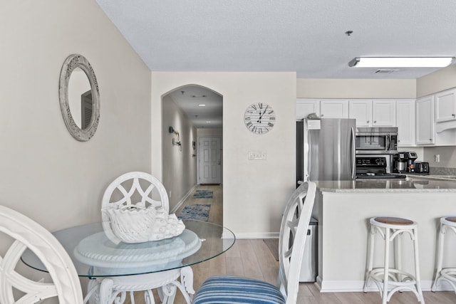 kitchen with appliances with stainless steel finishes, light hardwood / wood-style floors, a textured ceiling, white cabinets, and kitchen peninsula