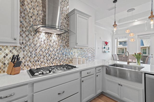 kitchen featuring a sink, appliances with stainless steel finishes, decorative backsplash, wall chimney exhaust hood, and a tray ceiling