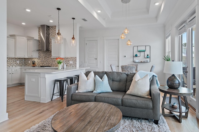 living room featuring ornamental molding, a tray ceiling, visible vents, and light wood-style flooring