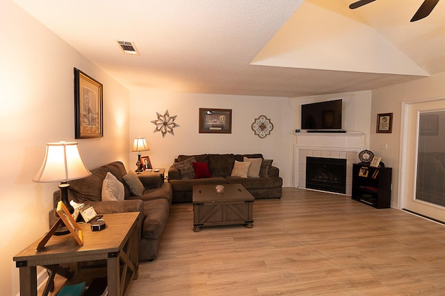 living room featuring ceiling fan, light hardwood / wood-style flooring, a tile fireplace, and a textured ceiling