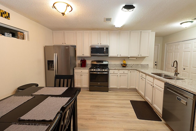 kitchen featuring sink, light hardwood / wood-style floors, stainless steel appliances, white cabinets, and light stone countertops