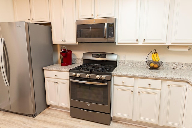 kitchen featuring appliances with stainless steel finishes, white cabinets, light stone countertops, and light hardwood / wood-style floors