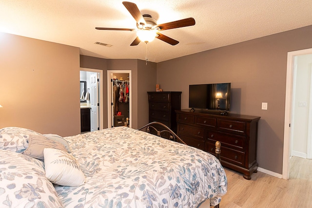 bedroom with a walk in closet, light hardwood / wood-style flooring, a closet, ceiling fan, and a textured ceiling