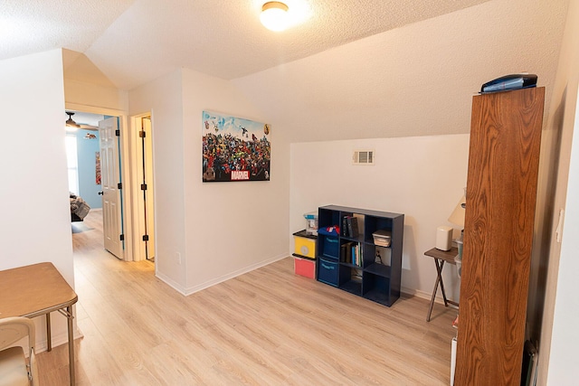 interior space featuring lofted ceiling, a textured ceiling, and light hardwood / wood-style flooring