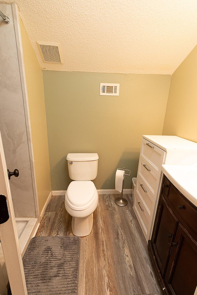 bathroom with toilet, wood-type flooring, a textured ceiling, walk in shower, and vanity