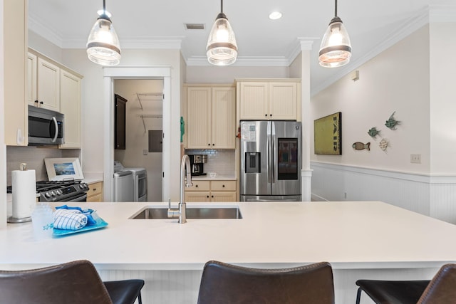 kitchen with appliances with stainless steel finishes, washer and clothes dryer, sink, and hanging light fixtures