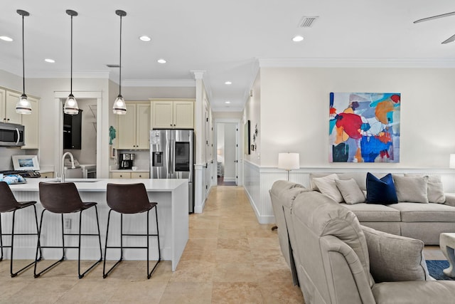 kitchen with a kitchen island, a breakfast bar, pendant lighting, stainless steel appliances, and cream cabinets