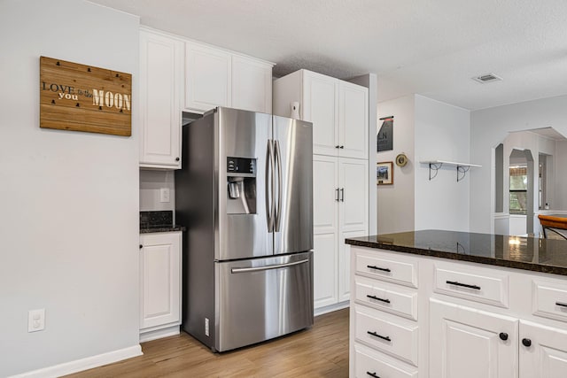 kitchen with visible vents, white cabinets, arched walkways, dark stone countertops, and stainless steel refrigerator with ice dispenser