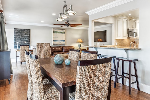 dining space featuring sink, dark wood-type flooring, ornamental molding, and ceiling fan