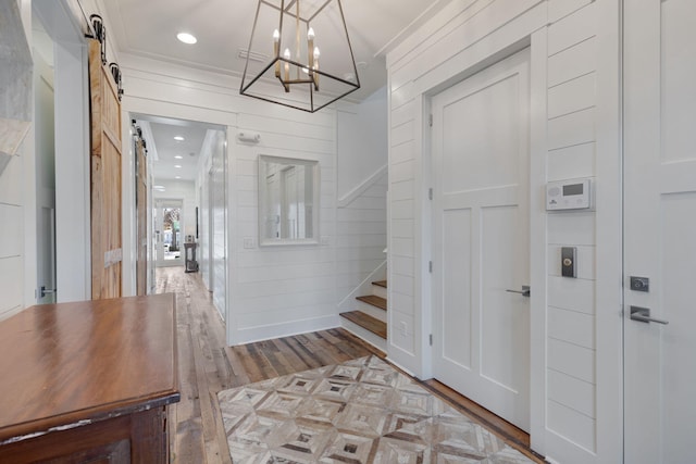 entrance foyer with crown molding, light hardwood / wood-style flooring, a barn door, and wood walls