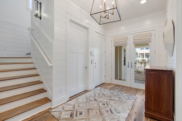 foyer entrance featuring hardwood / wood-style floors, crown molding, a notable chandelier, and french doors