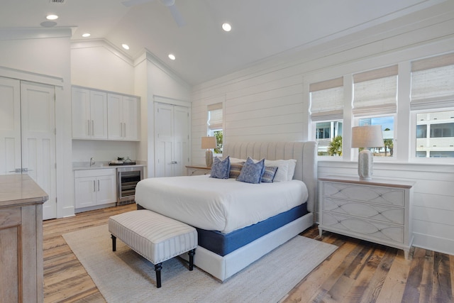 bedroom featuring indoor wet bar, wine cooler, wood-type flooring, vaulted ceiling, and multiple closets