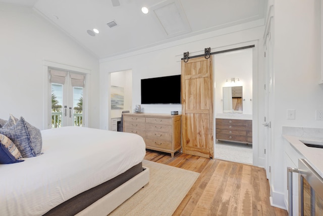 bedroom featuring lofted ceiling, access to exterior, ensuite bathroom, light hardwood / wood-style floors, and a barn door