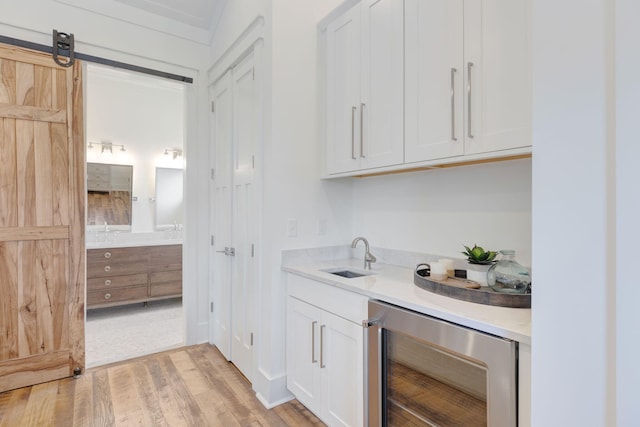 bar featuring white cabinetry, sink, beverage cooler, light hardwood / wood-style floors, and a barn door