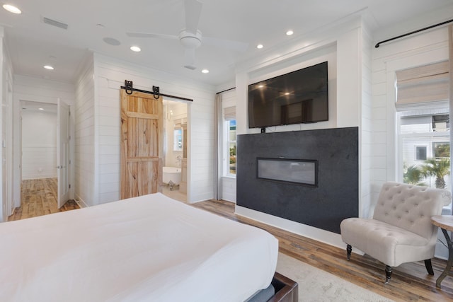 bedroom with a barn door, hardwood / wood-style floors, and ensuite bath