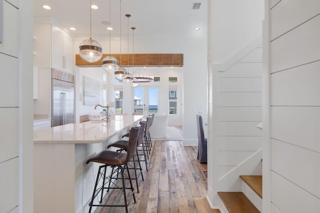 kitchen with a breakfast bar, decorative light fixtures, white cabinetry, stainless steel built in refrigerator, and light hardwood / wood-style floors