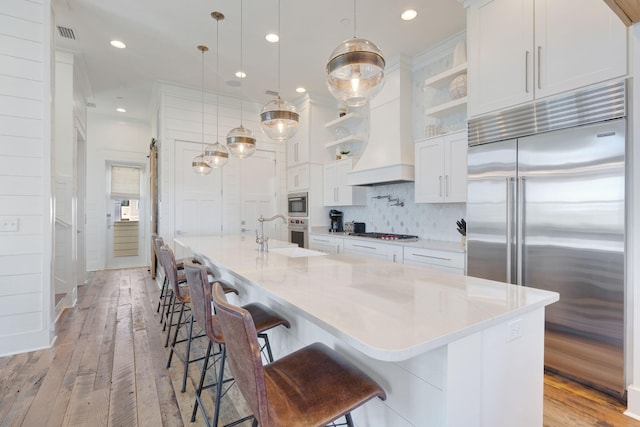 kitchen featuring a spacious island, a breakfast bar area, white cabinetry, built in appliances, and decorative light fixtures