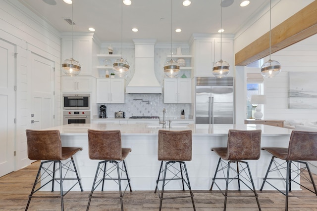 kitchen featuring stainless steel appliances, custom range hood, white cabinets, and a breakfast bar