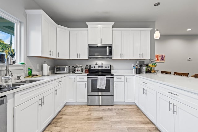 kitchen featuring pendant lighting, sink, stainless steel appliances, light hardwood / wood-style floors, and white cabinets