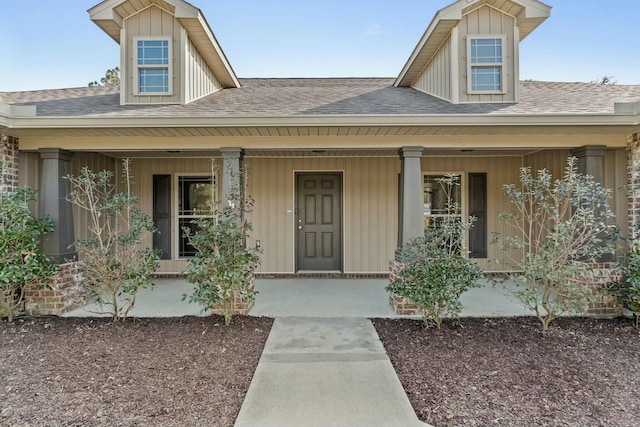 doorway to property with covered porch, roof with shingles, and board and batten siding