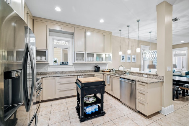 kitchen featuring sink, appliances with stainless steel finishes, light stone countertops, decorative light fixtures, and cream cabinetry