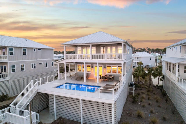 back house at dusk featuring a fenced in pool, a patio area, outdoor lounge area, and a balcony