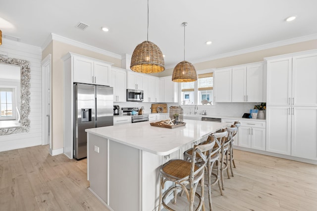 kitchen featuring decorative light fixtures, white cabinetry, a center island, stainless steel appliances, and crown molding