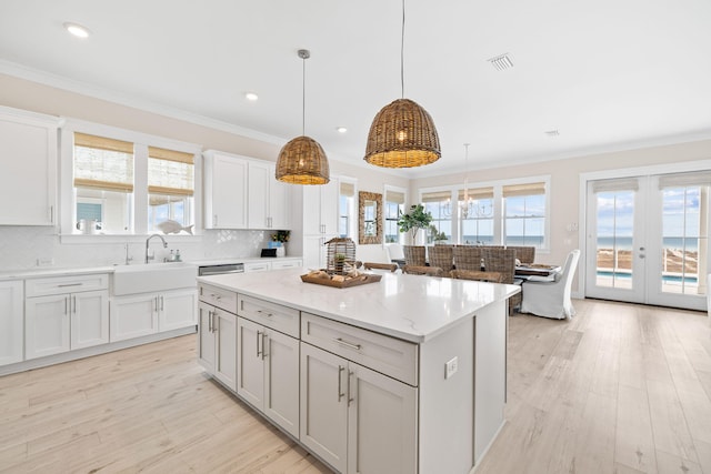 kitchen with a kitchen island, pendant lighting, sink, light stone counters, and french doors