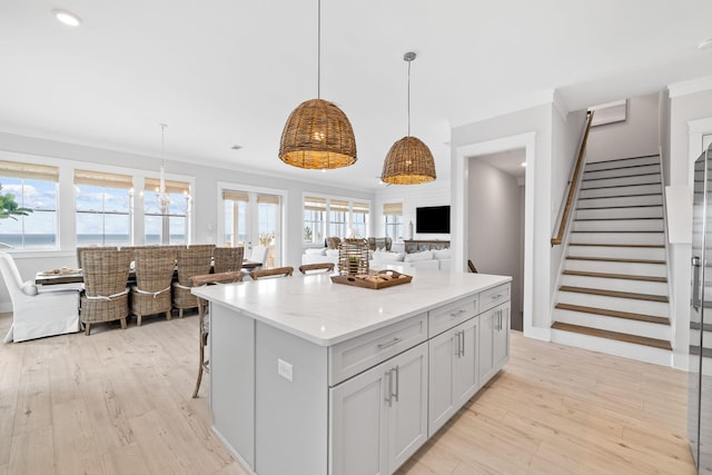 kitchen with a center island, light stone counters, ornamental molding, light hardwood / wood-style floors, and decorative light fixtures