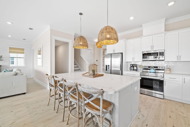 kitchen featuring a kitchen island, white cabinets, a kitchen breakfast bar, hanging light fixtures, and stainless steel appliances