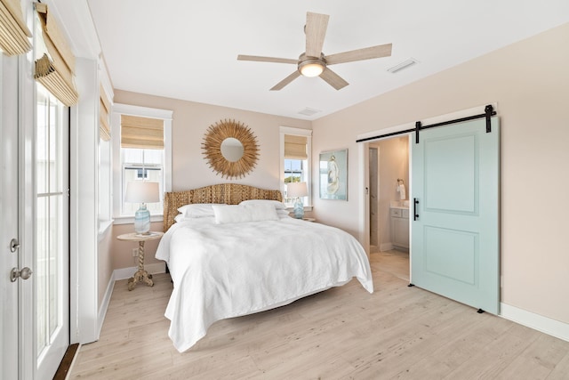 bedroom featuring ceiling fan, ensuite bath, a barn door, and light wood-type flooring