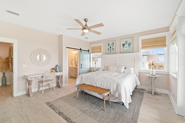 bedroom with ensuite bath, light hardwood / wood-style floors, a barn door, and ceiling fan