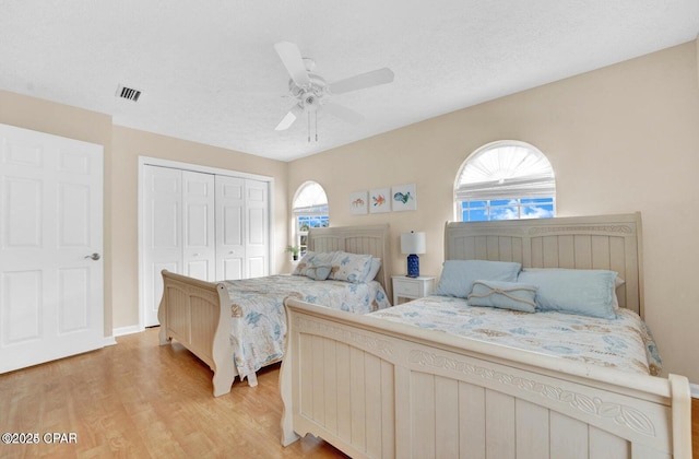 bedroom with ceiling fan, a closet, light hardwood / wood-style flooring, and a textured ceiling