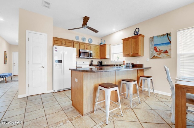 kitchen with light tile patterned flooring, a kitchen bar, ceiling fan, kitchen peninsula, and white appliances