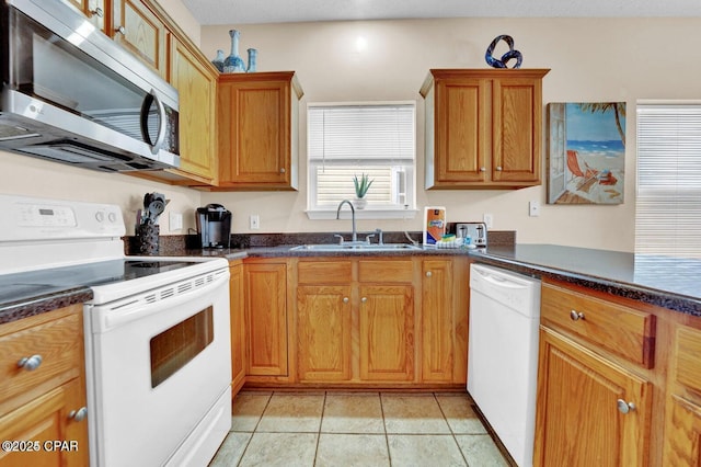 kitchen with light tile patterned flooring, sink, white appliances, and dark stone counters