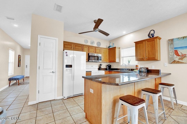 kitchen with ceiling fan, a breakfast bar, light tile patterned floors, and white appliances