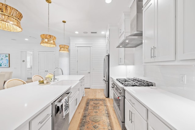 kitchen with white cabinets, appliances with stainless steel finishes, and wall chimney range hood