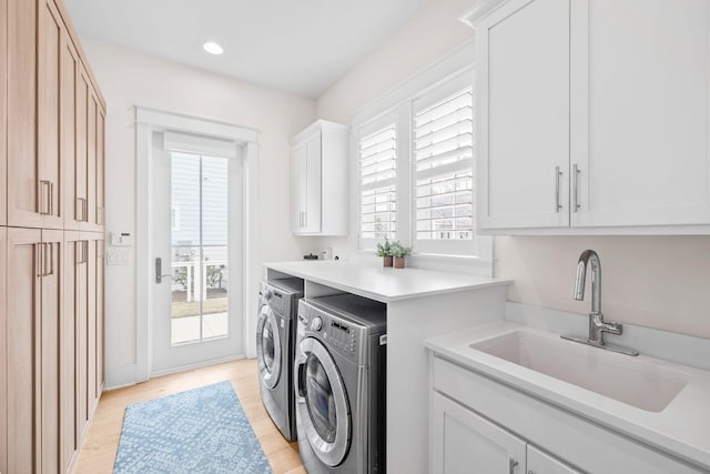 clothes washing area with sink, cabinets, washing machine and clothes dryer, and light wood-type flooring