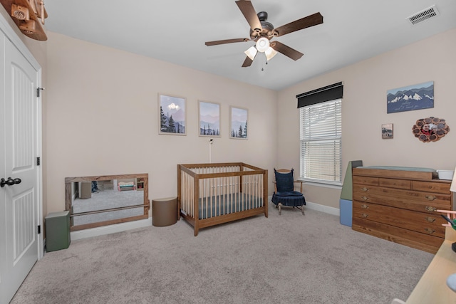 carpeted bedroom with a crib and ceiling fan