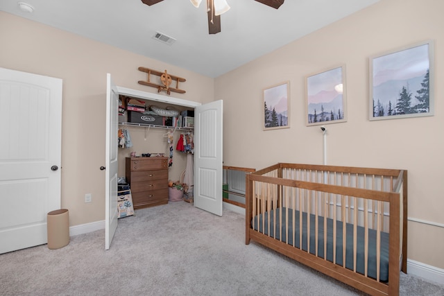 bedroom featuring a nursery area, light carpet, ceiling fan, and a closet