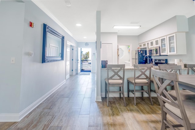 kitchen featuring appliances with stainless steel finishes, white cabinetry, kitchen peninsula, crown molding, and light hardwood / wood-style flooring