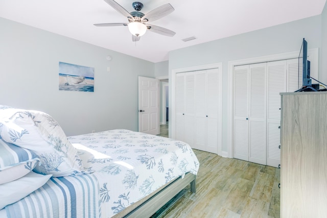 bedroom featuring ceiling fan, light hardwood / wood-style flooring, and two closets