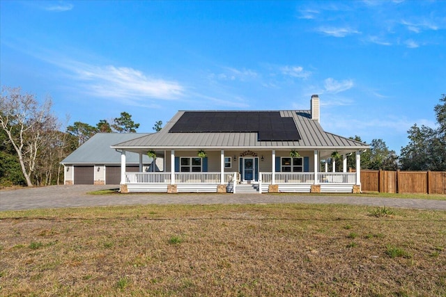 farmhouse inspired home with covered porch, solar panels, fence, a front lawn, and a chimney