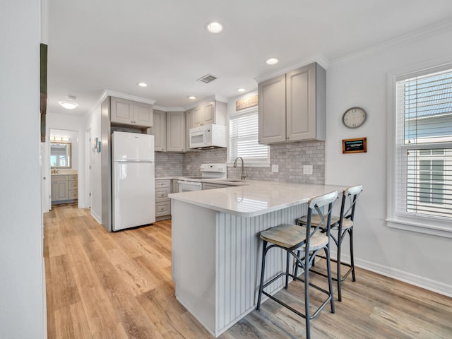 kitchen featuring a breakfast bar area, gray cabinetry, kitchen peninsula, white appliances, and light hardwood / wood-style floors