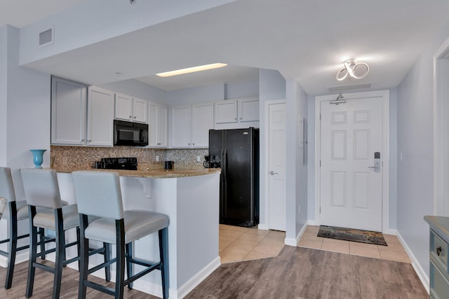 kitchen with visible vents, white cabinetry, black appliances, a peninsula, and a kitchen bar